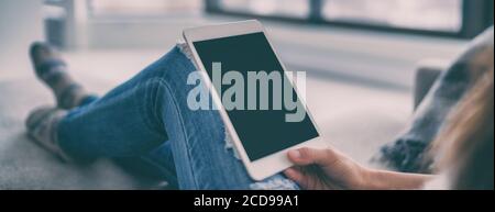 Woman using tablet relaxing at home watching movie sitting in sofa or shopping online holding pc device black screen empty copy space for advertising Stock Photo