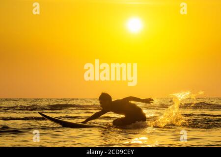 Surfing at Sunset. Outdoor Active Lifestyle. Summer water sport. Stock Photo