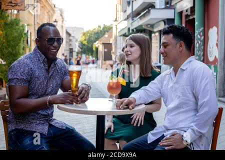 Multiracial group of friends drinking and laughing at street terrace of the cafe. Friendship concept with young multi ethnic people enjoying time toge Stock Photo