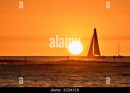 Spectacular and colorful golden sunset with silhouetted sailboat and surfers on horizon, Waikiki Beach, Oahu Island, Honolulu, Hawaii, USA Stock Photo