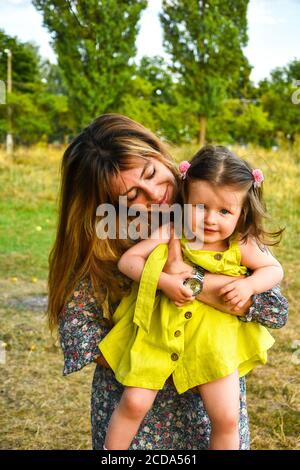 Young mother holding little baby girl kid on hands. Smiling and having fun in park. Autumn or summer weather. Family background Stock Photo