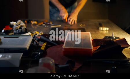 Tanner cuts out leather goods by cutter. Blurred background with man working by knife in dark workshop. Stock Photo