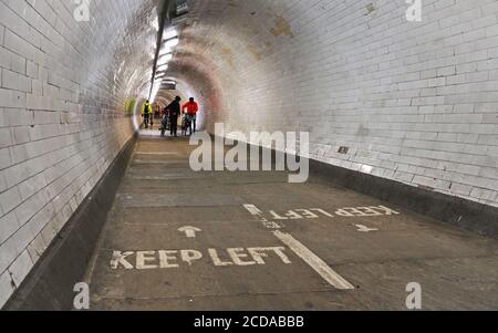 London, United Kingdom - February 02, 2019: Cyclists in bright jackets walking with their bicycles in Greenwich foot tunnel under river Thames, 'Keep Stock Photo