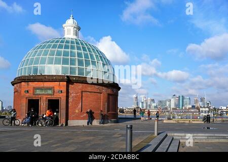 London, United Kingdom - February 02, 2019: Group of cyclists entering Greenwich foot tunnel under river Thames on sunny day, river and Canary Wharf d Stock Photo