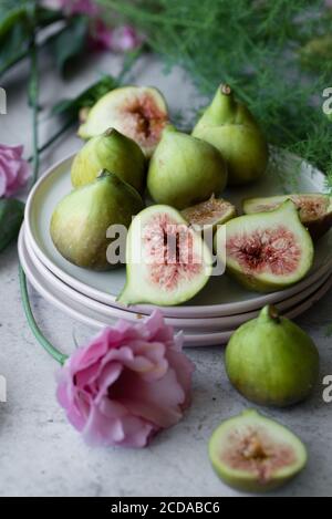 Ripe whole half and sliced figs among flavored green leaves of herbs and colorful flowers Stock Photo
