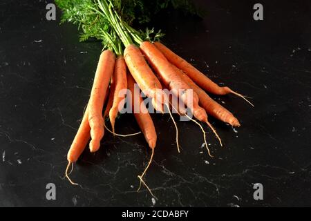 Bunch of organic raw carrot with green leaves on black marble like board, view from above Stock Photo
