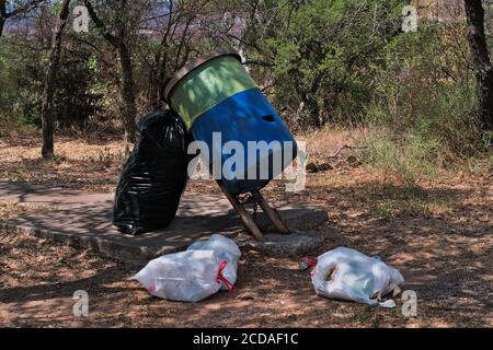 Trash spilling out top of barrel piled up bags around it dumped at a roadside rest stop causing pollution and enviromentally damaging ecosytem of habi Stock Photo