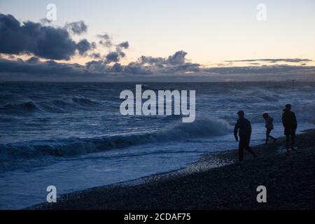 UK weather, 27 August 2020: At  East Wittering in West Sussex, strong winds and high surf pose a challenge for a family skimming stones into the waves at dusk. Anna Watson/Alamy Live News. Stock Photo