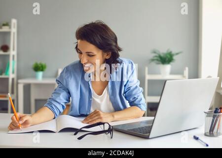 Smiling woman making notes during online lesson or meeting on laptop Stock Photo