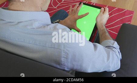 Man looks at the tablet sitting on the sofa, tablet with chromascreen Stock Photo