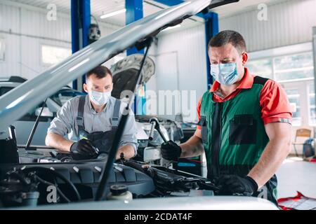 Mechanics in uniform and protective masks work in a car workshop. Stock Photo