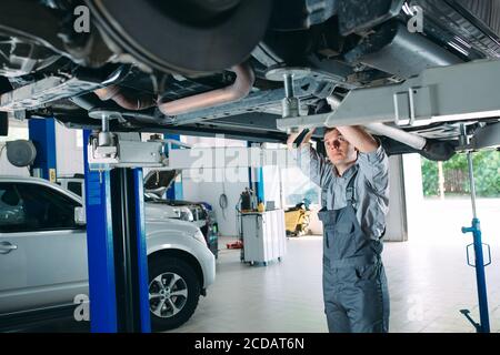 Portrait of a mechanic repairing a lifted car. Stock Photo