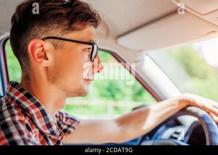 Young man in glasses driving car holding hand on wheel. Driver looking on road Stock Photo