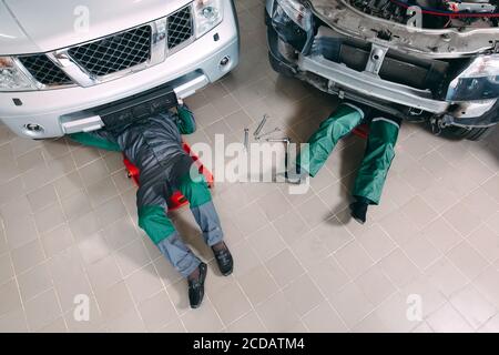 Mechanics in uniform lying down and working under car at the garage. Stock Photo
