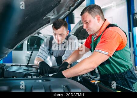 Two handsome mechanics in uniform are working in auto service. Car repair and maintenance. Stock Photo