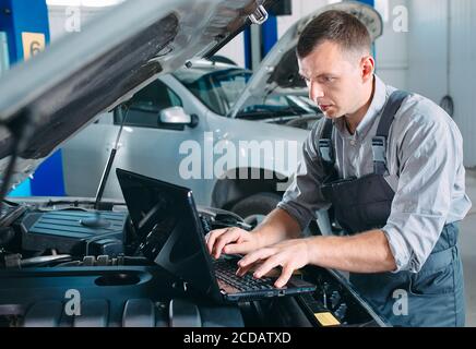 car mechanic using a computer laptop to diagnosing and checking up on car engines parts for fixing and repair. Stock Photo