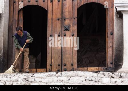 A Quiche Mayan man in modern dress sweeps the Mayan steps in front of the old wooden doorway of the Church of Santo Tomas in Chichicastenango, Guatema Stock Photo