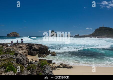 Tourists watch waves from the Atlantic Ocean crash on the limestone shore of the peninsula of Pointe des Chateaux on the island of Grande-Terre, Guade Stock Photo