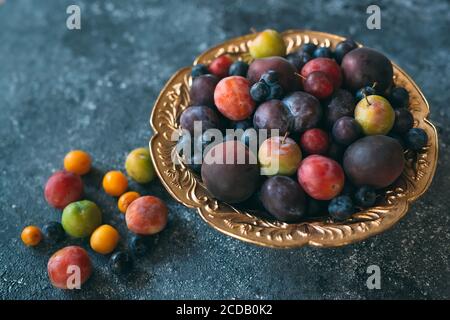 Multicolored plums on a plate are laid out by color. Stock Photo