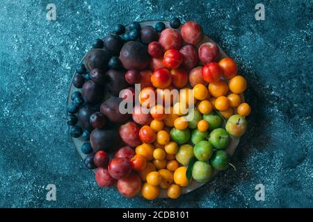 Multicolored plums on a plate are laid out by color. Stock Photo