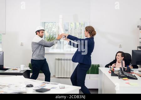 Young people having fun in the office during after hours. Pretanding they are fighting with swards. Stock Photo