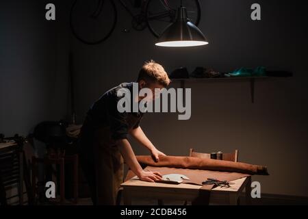 a young man is engaged in the family craft of making leather shoes in a workshop Stock Photo