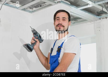 The man holds a drill in his hands. He is wearing blue overalls Stock Photo