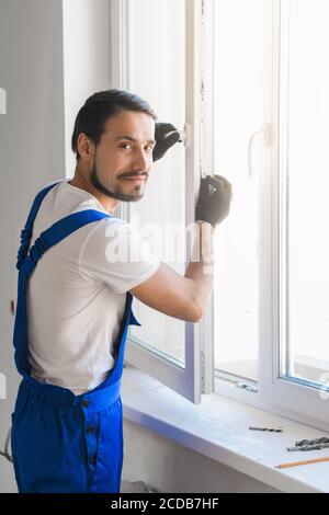 Male construction worker in overalls installs a window and poses at the camera Stock Photo