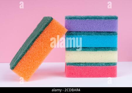 Multicolored sponges for washing dishes on top of each other on a pink background. Cleaning concept. Stock Photo