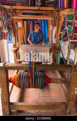 A Cakchiquel Mayan woman in the traditional dress of San Antonio Palopo, Guatemala weaves colorful fabric on a traditional wooden foot-treadle loom. Stock Photo
