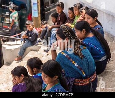 A Cakchiquel Mayan woman and children watch a program from the steps of the church in San Antonio, Palopo, Guatemala.   The woman and girls wear the t Stock Photo