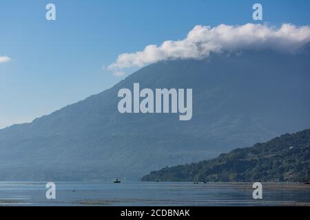 Mayan fishermen paddle their cayucos or canoes on Lake Atitlan by San Pedro la Laguna, Guatemala.  The summit of Toliman Volcano is covered in clouds Stock Photo