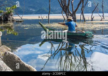 A fisherman paddles his cayuco on Lake Atitilan at San Pedro la Laguna, Guatemala.  Standing dead trees reflect in the calm water.  Lake level has ris Stock Photo
