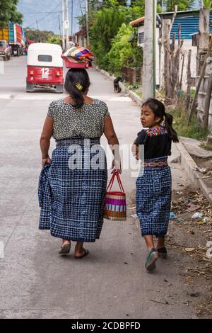 A Mayan mother and daughter in traditiional dress walk towards home in San Pedro la Laguna, Guatemala.  The woman balances a bowl of fresh tortillas o Stock Photo