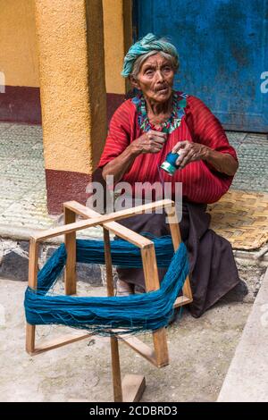 An older Cakchiquel Mayan woman in traditional dress winds thread on a frame to prepare for weaving on a back loom in Santa Cruz la Laguna, Guatemala. Stock Photo