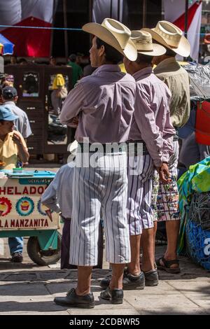 Three Tzutujil Mayan men in traditional dress , including the knee-length striped pants, in the weekly market in Santiago Atitlan, Guatemala. Stock Photo