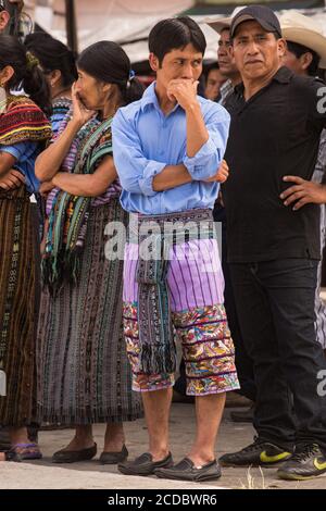 Two Tzutujil men, one in traditional dress, wait for the dancers to perform in the festival of Santiago in Santiago Atitlan, Guatemala. Stock Photo