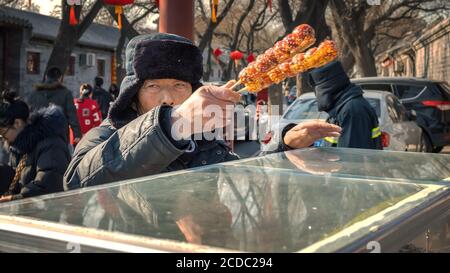 Beijing, China - Jan 12 2020: Unidentified street vendor sells Tanghulu - a Northern Chinese traditional sweet in front of the Temple of Confucius Stock Photo
