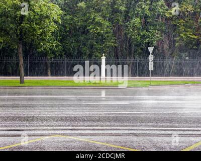 city street in heavy rain. torrential summer rain on green park trees background Stock Photo