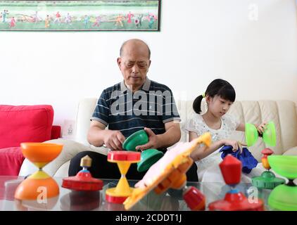 (200828) -- BEIJING, Aug. 28, 2020 (Xinhua) -- Dong Shulin (L) and his granddaughter Dong Yutong clean and fix diabolos at home in Beijing, capital of China, Aug. 11, 2020. Dong Shulin, 66, lives with his wife Mei Yongpei and his 9-year-old granddaughter Dong Yutong in Beijing. Dong Shulin started to play diabolo in 2003 and now the whole family are fond of playing this traditional folk game, in which one can throw and catch a spinning top by moving a cord fastened to two sticks. In Dong Shulin's home, over 70 diabolos were placed all around. Some of the diabolos were purchased and others were Stock Photo