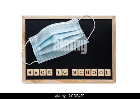 Back to school words lettering on the school black chalkboard. Medical mask on the background of the chalkboard. The concept of social distance. Flat Stock Photo