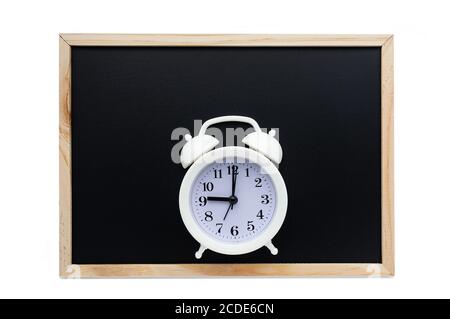 White alarm clock on the background of a black school board. The concept of the beginning of the school year. Flat lay. Copy space. Stock Photo
