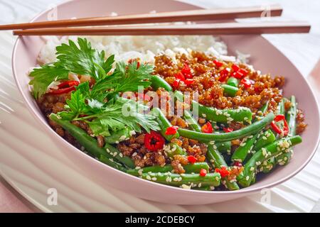 Thai pad kra pao: stir-fried pork with long grain rice and green beans sprinkled with sesame seed, red chili served on a pink bowl with chopsticks on Stock Photo