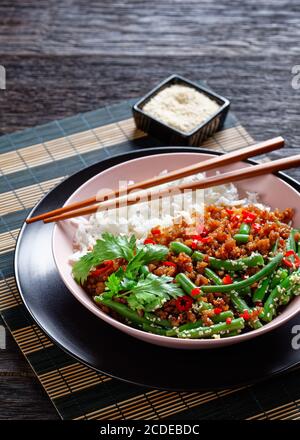 Asian basil minced pork pad kra pao with long grain rice and green beans sprinkled with sesame seed, red chili served on a pink bowl with chopsticks o Stock Photo