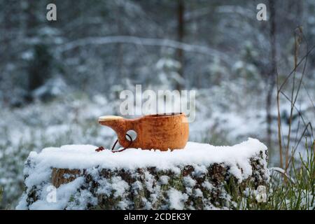A wooden cup with tasty coffee stands on a stump in the winter forest. Stock Photo