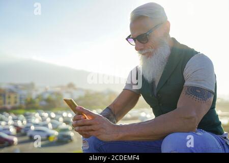 Trendy senior man using smartphone app - Mature fashion male having fun with new trends technology - Tech and joyful elderly lifestyle concept - Focus Stock Photo