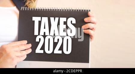 Taxes 2020 words on black notepad in businesswoman hands. business concept Stock Photo
