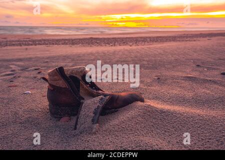 Old used boot lie half buried in desert sand dune in the evening light Stock Photo