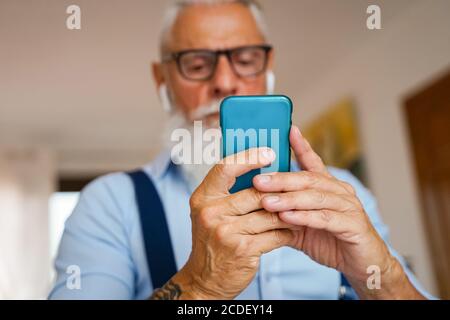 Attractive man in the house, changes songs and tracks on smartphone, listens to music in wireless headphones. Man with beard. focus hands - Image Stock Photo