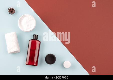 Skin care products on brown and blue surface. Frame from shampoo or cosmetic lotion bottle, towel, open facial cream jar. Beauty concept. Flat lay Stock Photo